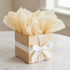 Beautifully wrapped luxury gift box with ivory cream tissue paper overflowing elegantly, white satin ribbon, marble surface