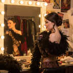 Woman wrapping a black feather boa around her shoulders at a burlesque dressing room vanity mirror