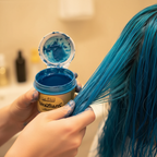 Hands applying La Riche Directions Lagoon Blue hair dye to vibrant blue hair, candid application moment with bokeh background