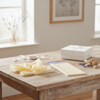 Ivory tissue paper pack on a wooden gift wrapping table with white ribbon, gift box and dried flowers, natural window light