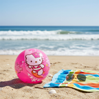 Hello Kitty pink beach ball resting on golden sand beside beach towel and sunglasses, natural light