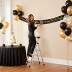 Woman hanging 9ft black and gold 70th birthday banner at elegant party celebration