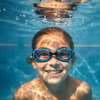 Child underwater in clear blue pool wearing Osprey swimming goggles smiling at camera
