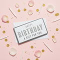 Flat lay of Happy Birthday money wallet and envelope on pink background with gold confetti and candles