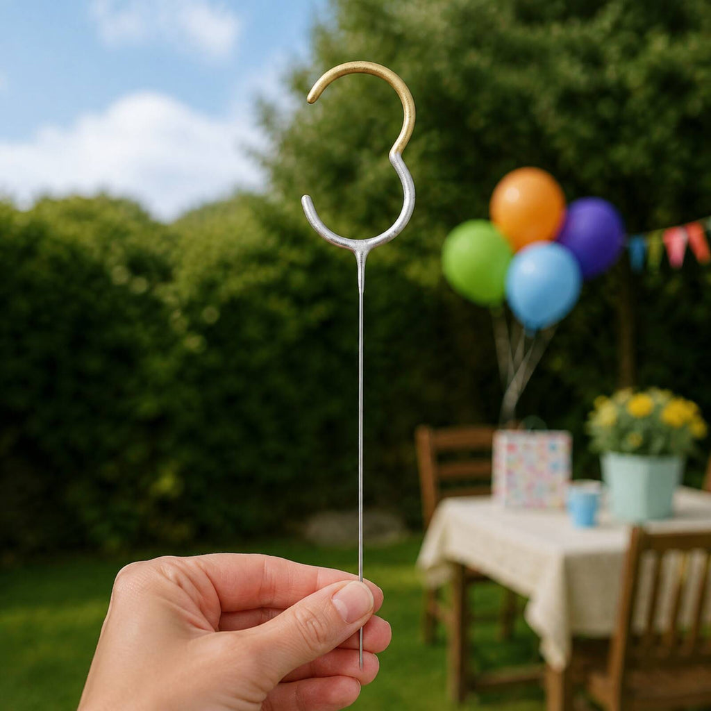 Adult safely holding the stem of an unlit number 3 gold and silver birthday sparkler outdoors