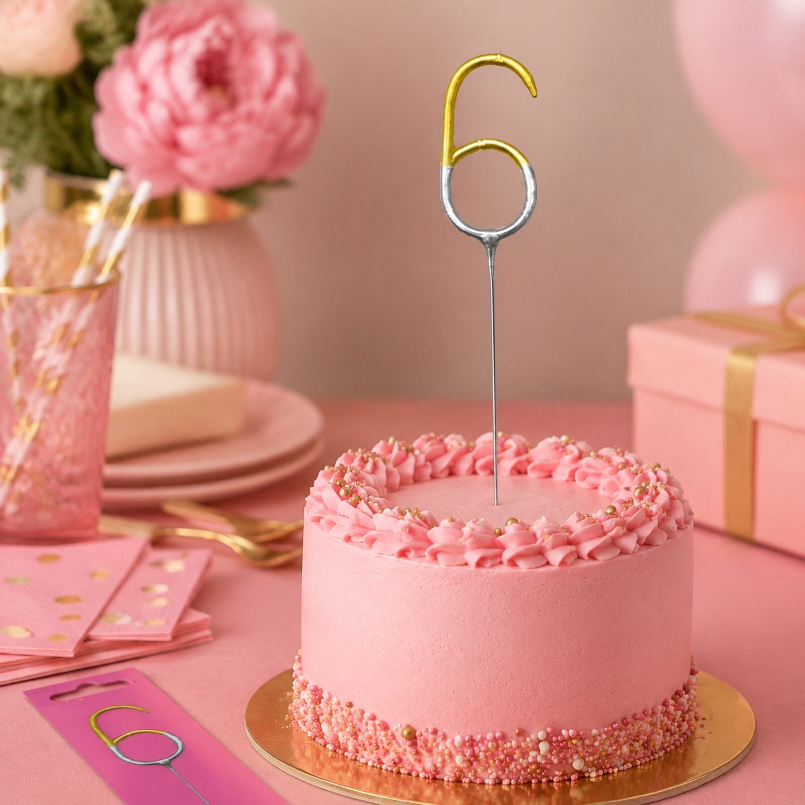 Unlit number 6 gold and silver sparkler displayed on a pink birthday party cake