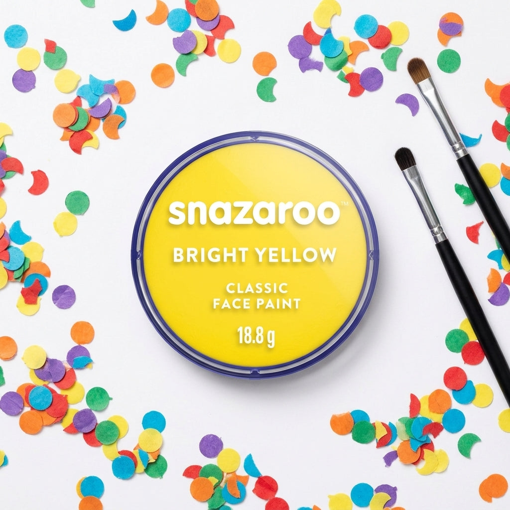 A round tin of Snazaroo Bright Yellow Classic Face Paint is centered on a white background, surrounded by colorful confetti and two makeup brushes. The tin label is bright yellow with white text, and the brushes have black handles and silver ferrules.