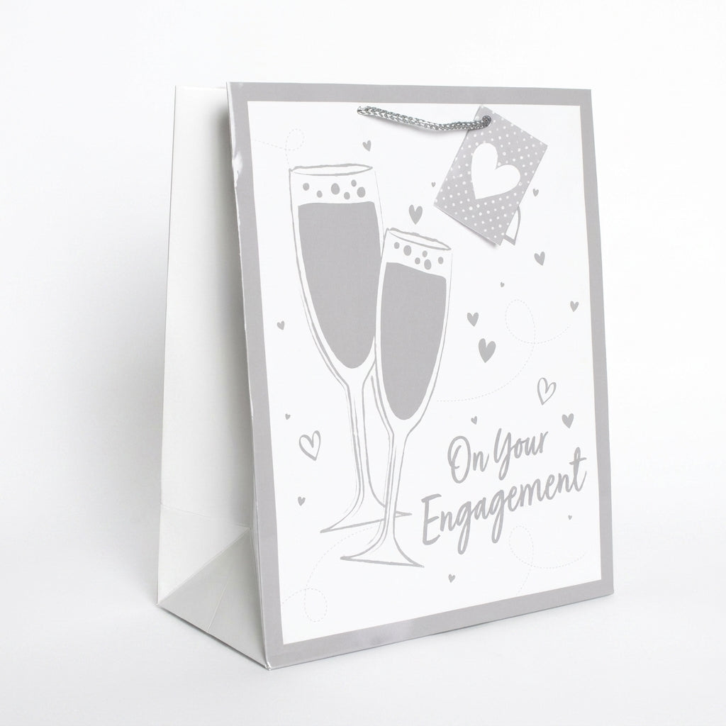 A white and silver gift bag with a champagne-themed design, featuring two champagne glasses, small hearts, and the text 'On Your Engagement'.