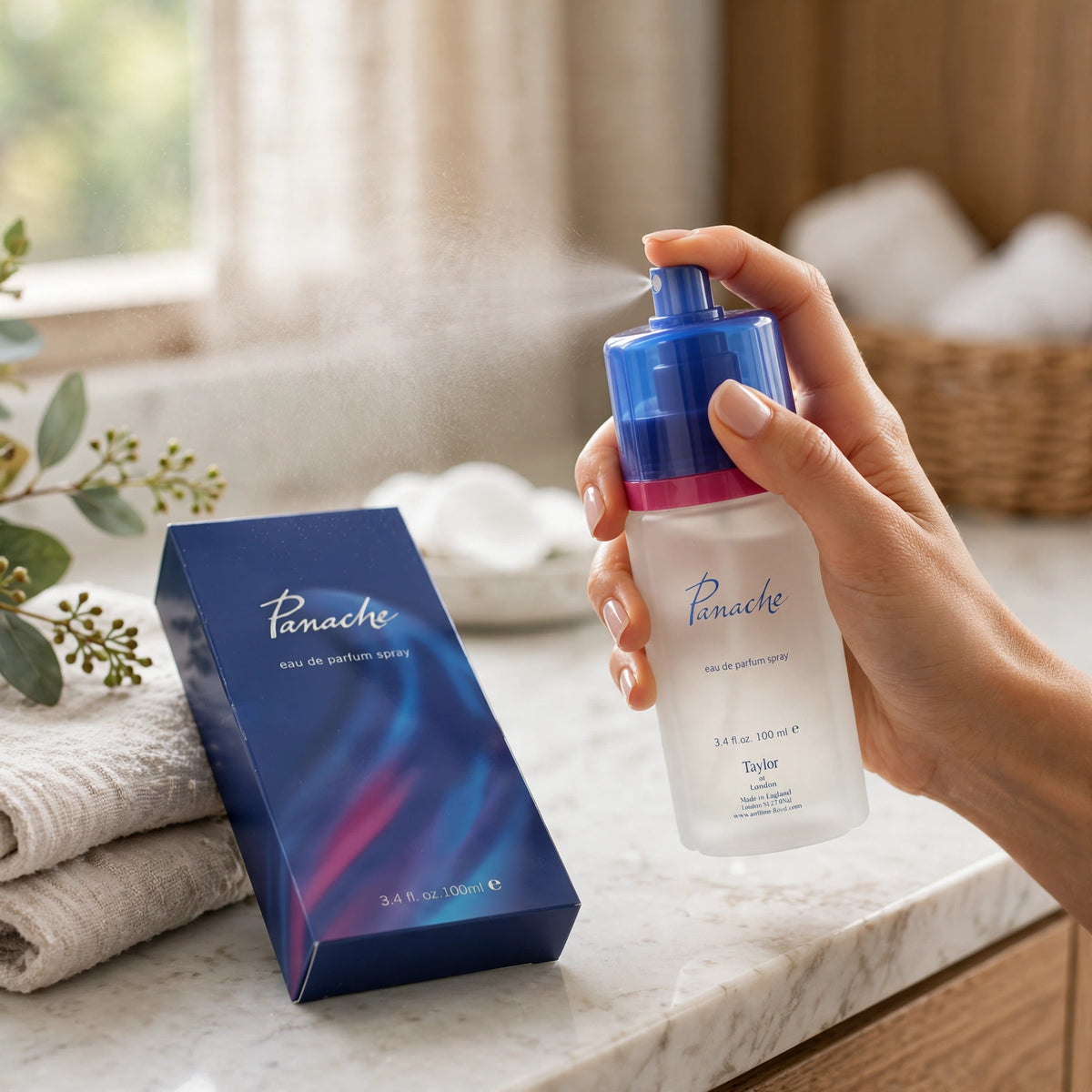 Lifestyle: Hand spraying Taylor of London Panache perfume beside its blue box and folded towels on a bathroom counter.